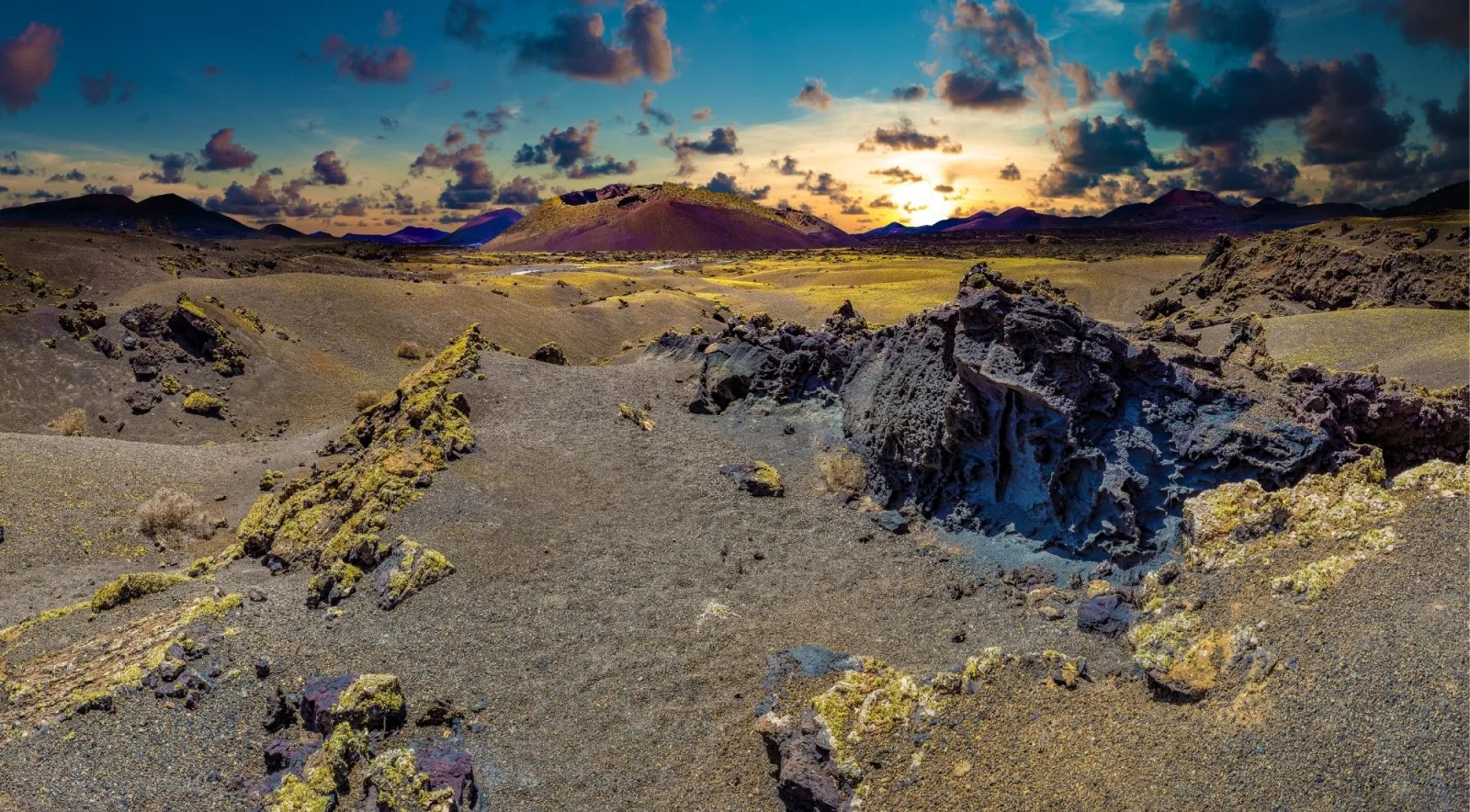 Sunset over the black lava fields of Timanfaya, a cinder cone silhouetted against an orange sky