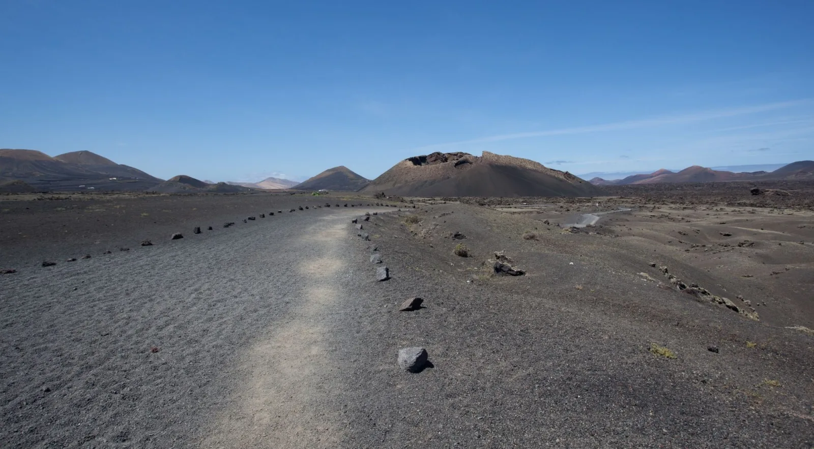 A stone-lined footpath crossing black volcanic gravel towards a line of cinder cones