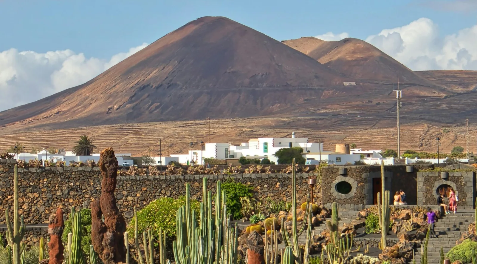 A dark volcanic cone above a white Lanzarote village and a dry-stone lava wall
