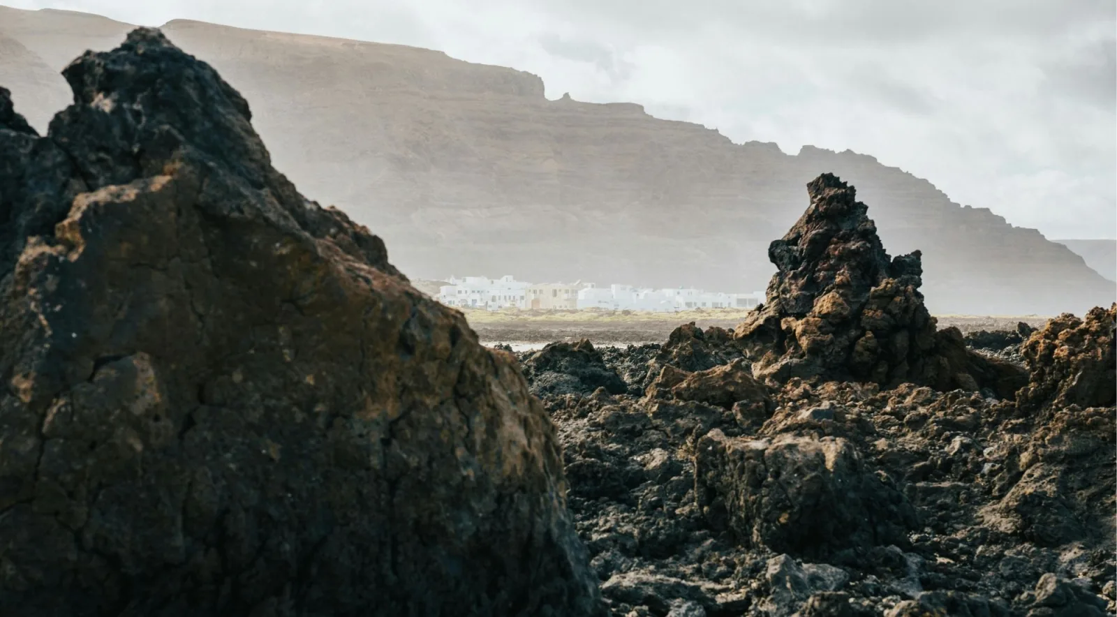 Jagged black lava boulders in the foreground with the Famara cliffs hazy behind