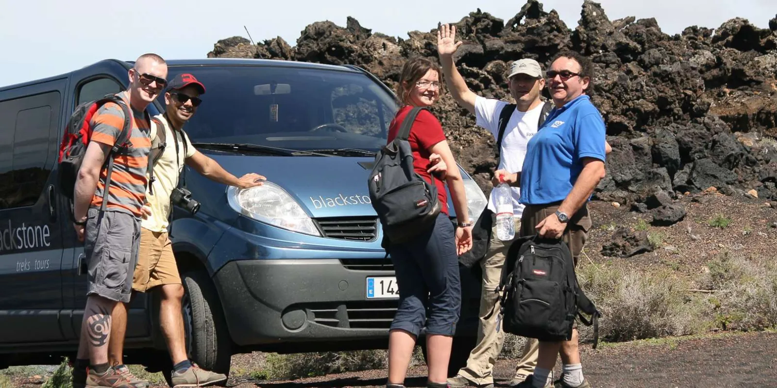 A small group and their guide beside the operator's minibus at the edge of the lava field