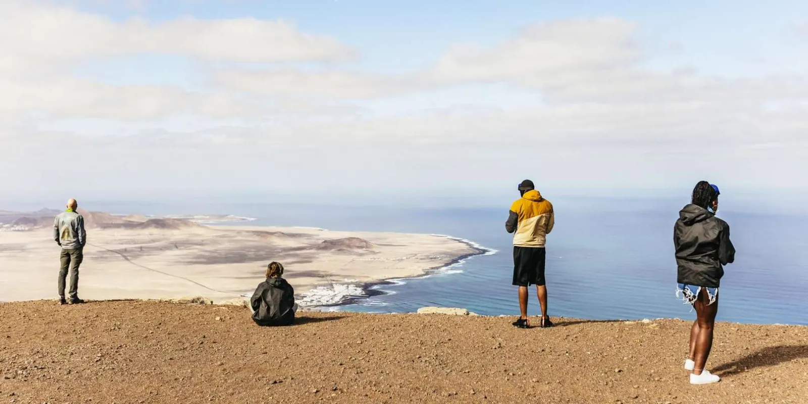 Riders at a clifftop viewpoint looking down over La Graciosa and the Famara coast