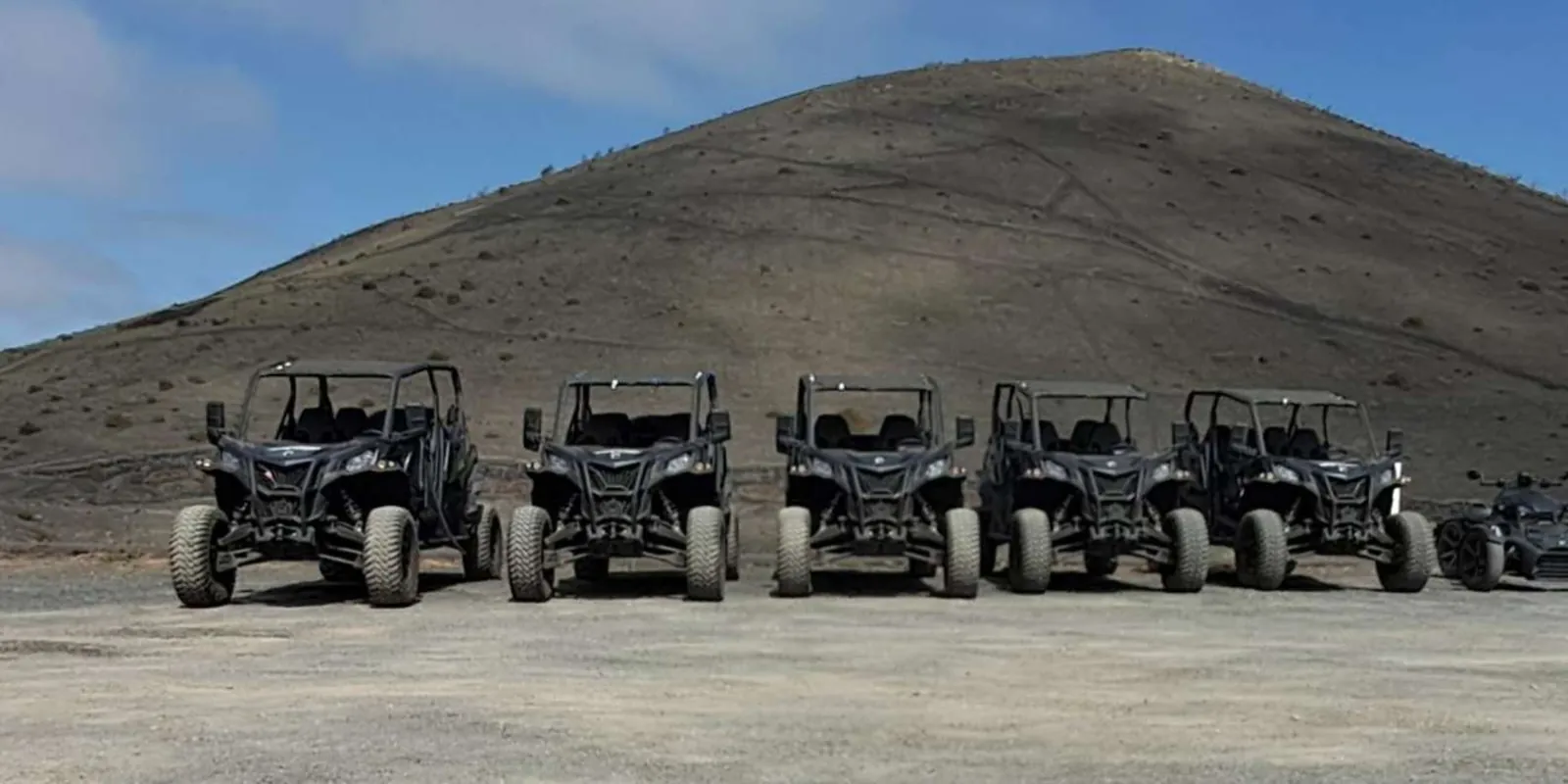 Five buggies lined up on volcanic gravel in front of a cinder cone