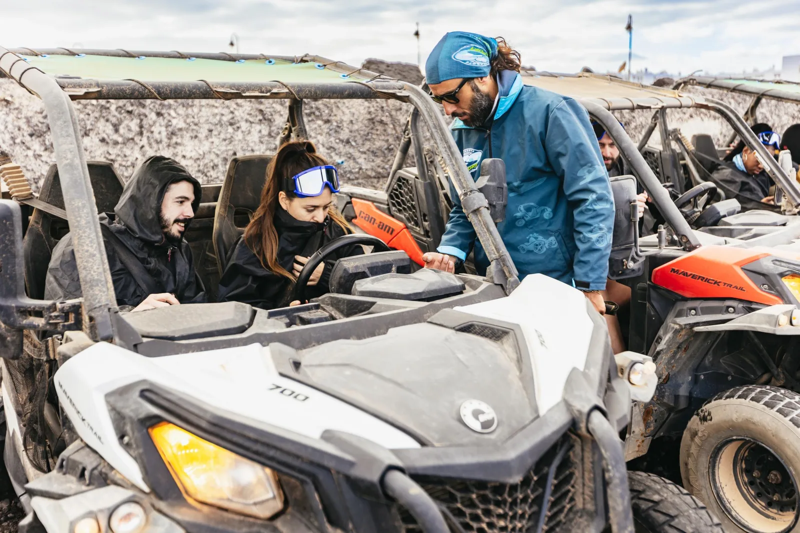 A guide briefing two drivers in goggles at the wheel of a Can-Am buggy before the tour