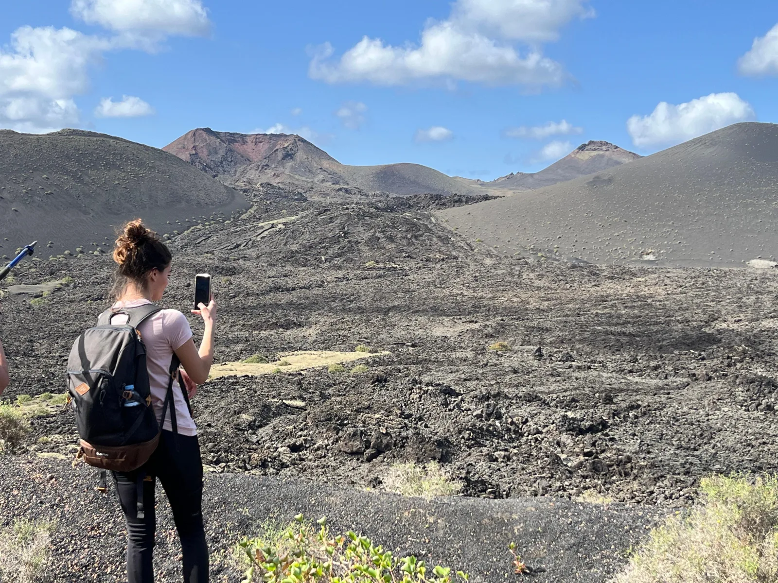 A hiker photographing a black lava flow with volcanic cones behind, Volcanes Natural Park, Lanzarote