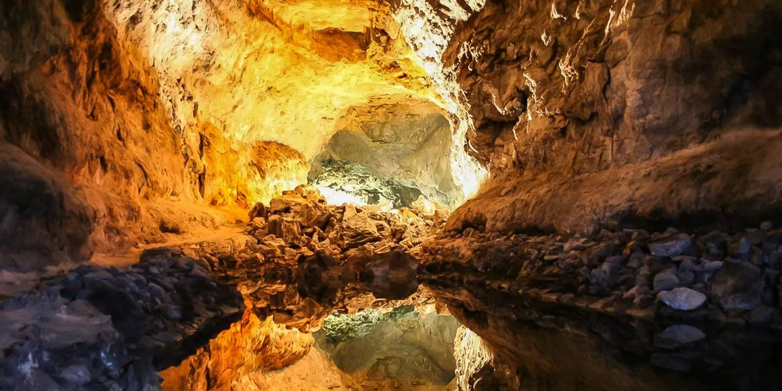 Floodlit chamber of the Cueva de los Verdes lava tube reflected in still water