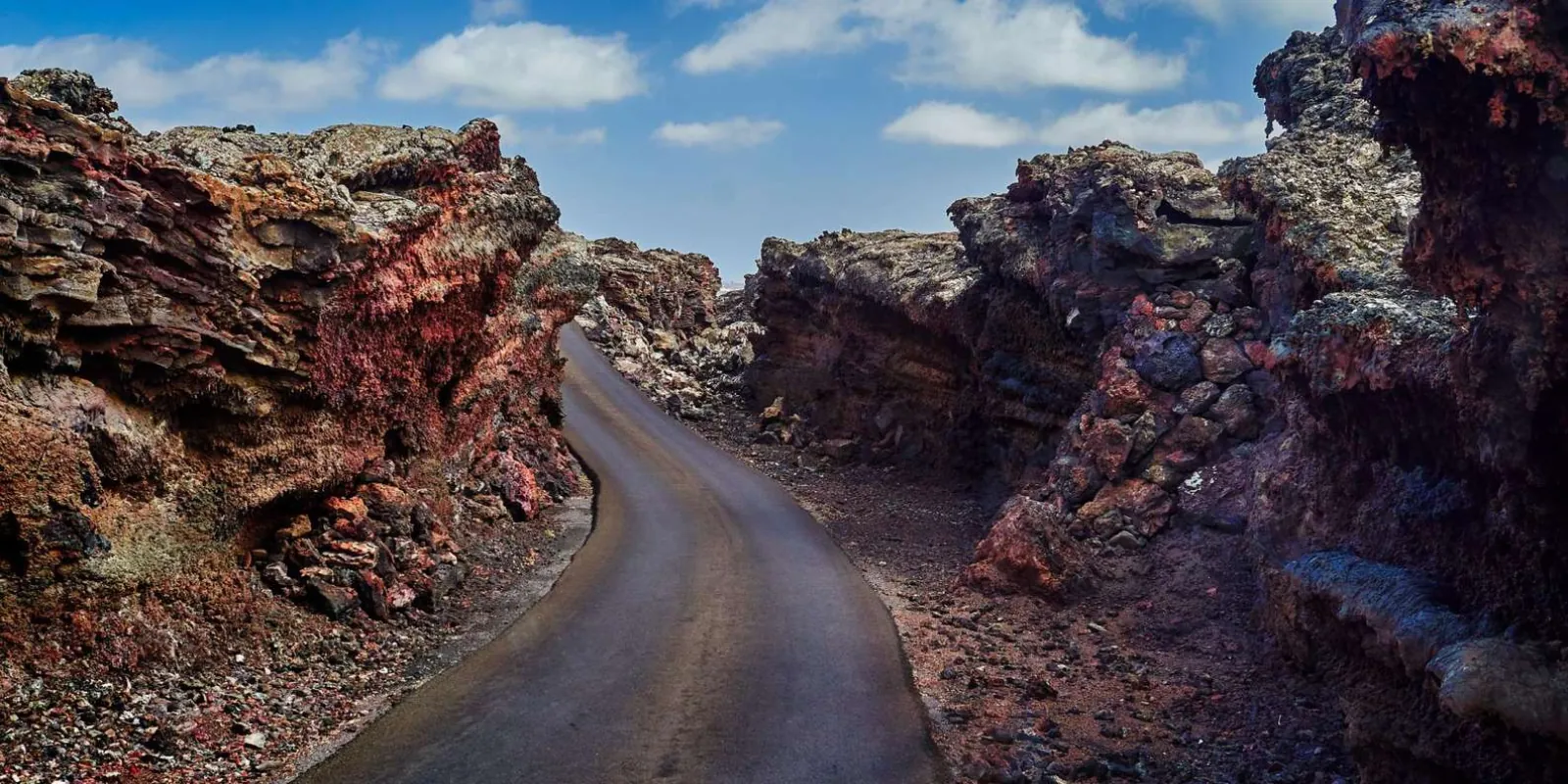 A narrow road cut through red and black lava rock in Timanfaya National Park